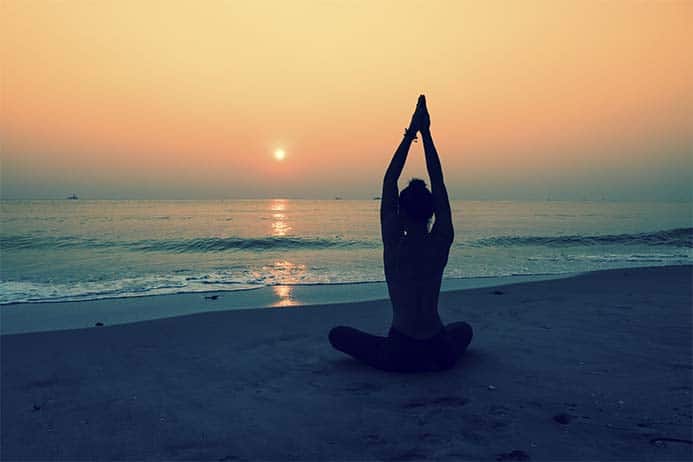 garota fazendo posição de yoga e meditando em frente ao mar num lindo pôr do sol