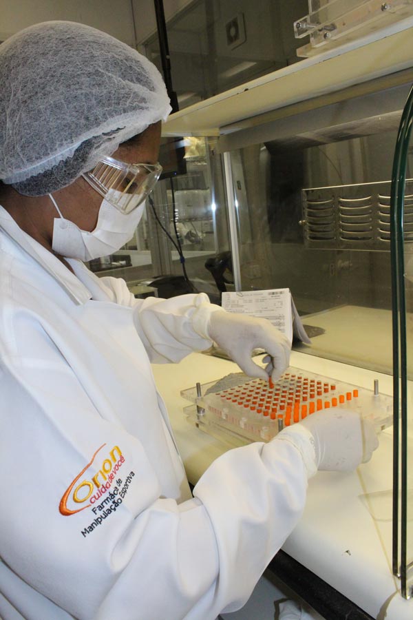 Profissional em ambiente de laboratório da Órion Farmácia de Manipulação, vestindo equipamentos de proteção individual, realizando o processo de encapsulação manual de fórmulas. A imagem destaca o rigor, a precisão e o cuidado na produção de medicamentos personalizados, reforçando o compromisso da Órion com a qualidade e segurança de suas manipulações.