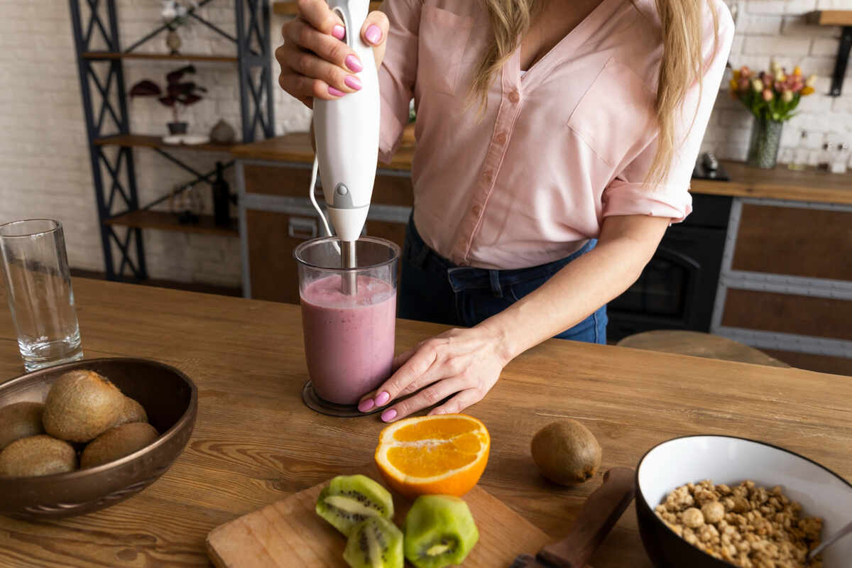 Mulher preparando um smoothie saudável com frutas frescas como kiwi e laranja na cozinha, representando escolhas alimentares que promovem a saúde metabólica e auxiliam no emagrecimento, complementadas pelos produtos da Órion Farmácia de Manipulação