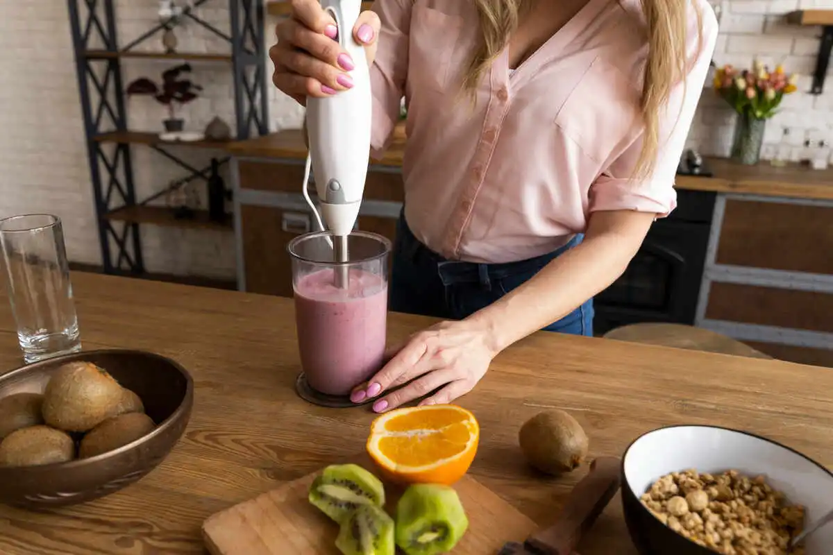 Mulher preparando um smoothie saudável com frutas frescas como kiwi e laranja na cozinha, representando escolhas alimentares que promovem a saúde metabólica e auxiliam no emagrecimento, complementadas pelos produtos da Órion Farmácia de Manipulação