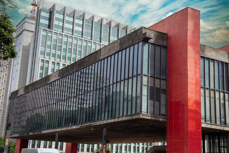 Fachada externa do Museu de Arte de São Paulo (MASP), um edifício icônico com sua estrutura suspensa, grandes janelas de vidro e pilares de concreto vermelho vibrante, destacando a arquitetura moderna na paisagem urbana de São Paulo. A imagem representa o ambiente dinâmico das grandes cidades, onde a Órion Farmácia de Manipulação oferece soluções personalizadas para a saúde e bem-estar.